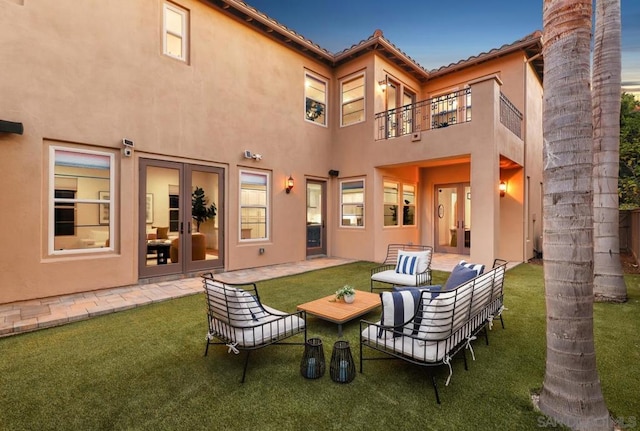 back house at dusk featuring a yard, a balcony, an outdoor living space, and a patio area