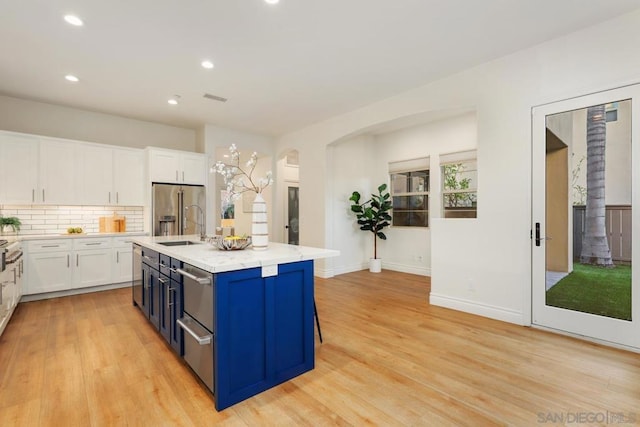 kitchen featuring a kitchen island with sink, a breakfast bar area, blue cabinetry, high end fridge, and white cabinetry