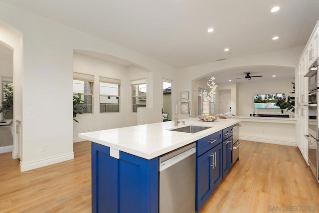 kitchen with stainless steel appliances, an island with sink, blue cabinetry, ceiling fan, and sink