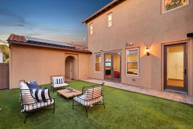 back house at dusk featuring solar panels, a patio, a yard, and outdoor lounge area