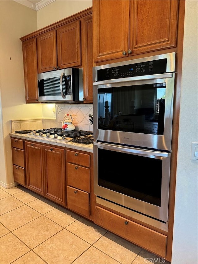 kitchen with stainless steel appliances, light tile patterned flooring, decorative backsplash, and tile counters