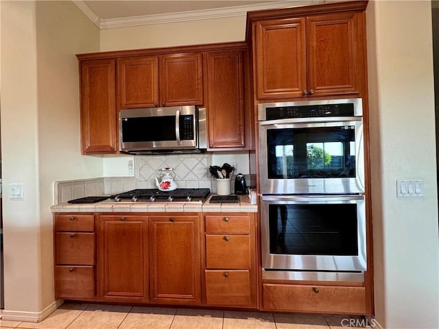 kitchen featuring tile counters, stainless steel appliances, light tile patterned floors, ornamental molding, and tasteful backsplash