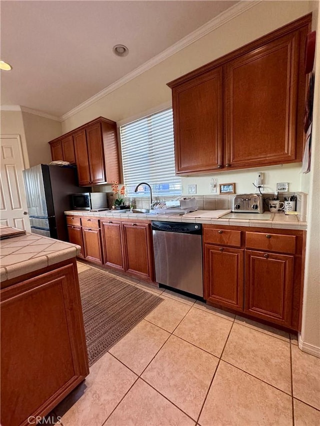 kitchen with tile counters, light tile patterned floors, crown molding, appliances with stainless steel finishes, and sink