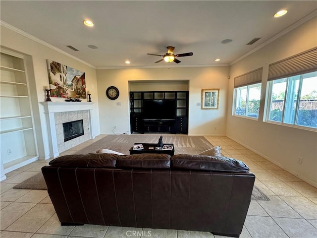 tiled living room with a tiled fireplace, built in features, ceiling fan, and ornamental molding