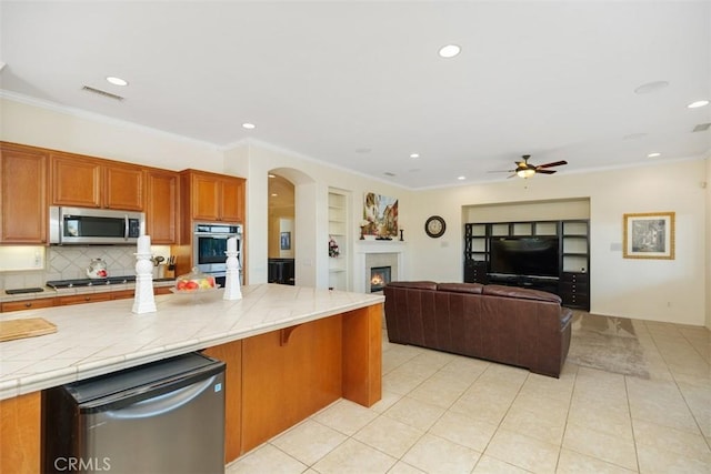 kitchen with tile countertops, ceiling fan, ornamental molding, built in features, and appliances with stainless steel finishes