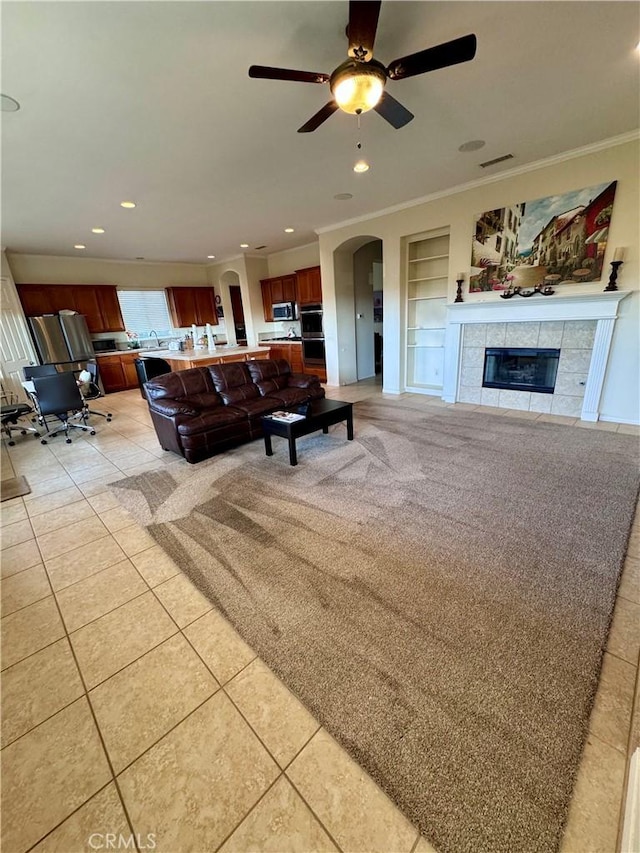 living room featuring a fireplace, ornamental molding, ceiling fan, light tile patterned floors, and built in features