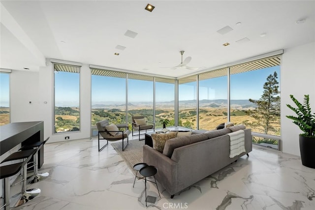 living room featuring ceiling fan, a wall of windows, and a mountain view