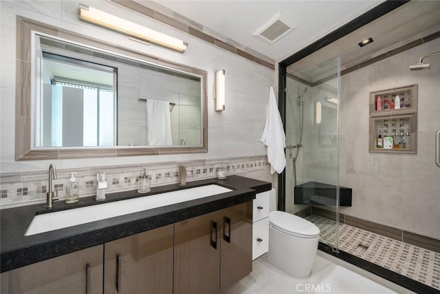 bathroom with toilet, a shower with door, tile patterned flooring, tile walls, and vanity