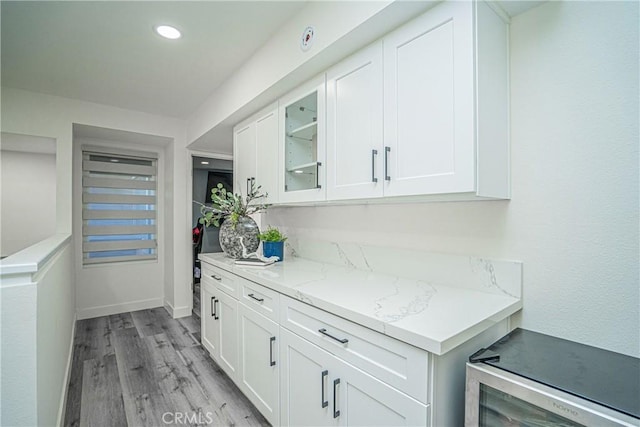 bar featuring white cabinets, light hardwood / wood-style floors, and light stone countertops