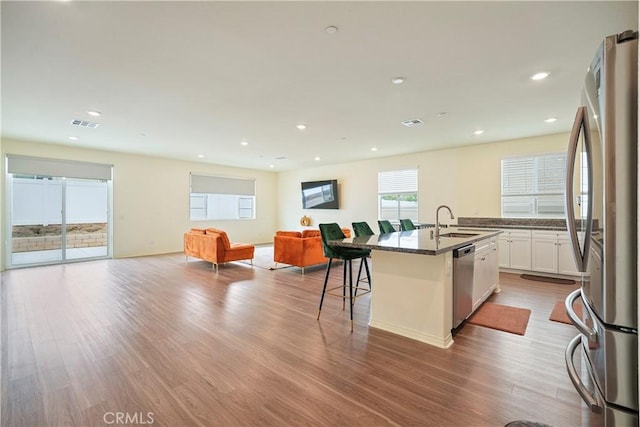 kitchen featuring white cabinets, a kitchen bar, light wood-type flooring, a kitchen island with sink, and appliances with stainless steel finishes