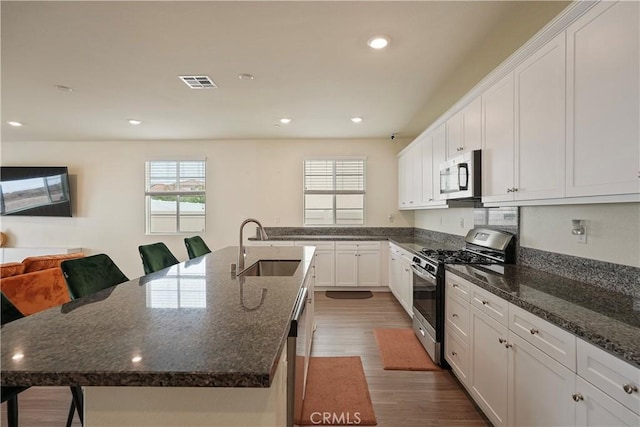 kitchen featuring dark stone countertops, appliances with stainless steel finishes, an island with sink, sink, and white cabinetry