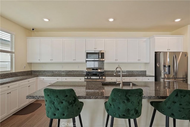 kitchen with appliances with stainless steel finishes, white cabinets, a breakfast bar area, and sink