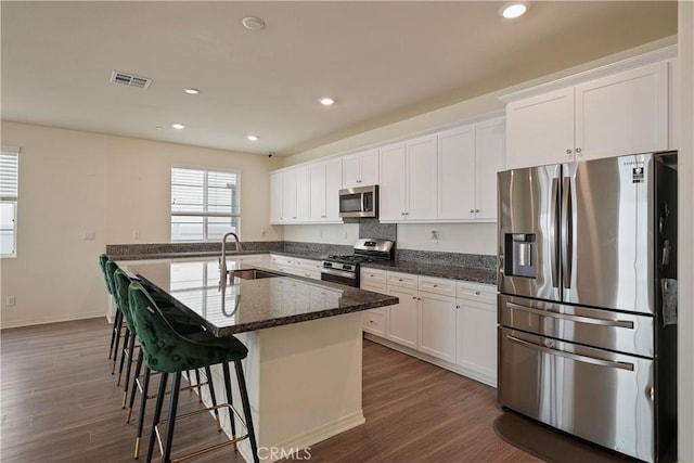 kitchen featuring dark stone countertops, appliances with stainless steel finishes, a breakfast bar, sink, and white cabinetry