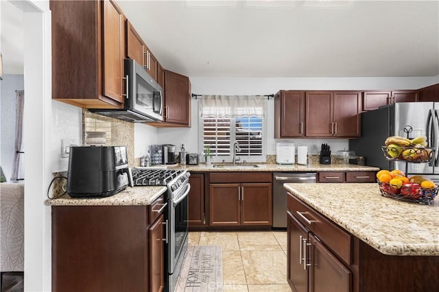 kitchen with appliances with stainless steel finishes, decorative backsplash, sink, light stone counters, and light tile patterned flooring