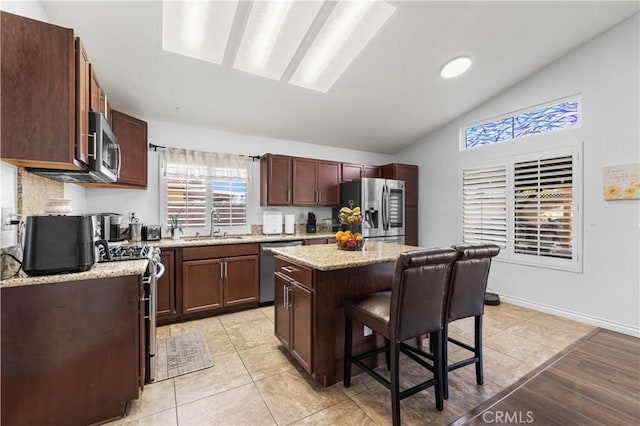 kitchen with a center island, stainless steel appliances, sink, a kitchen breakfast bar, and vaulted ceiling