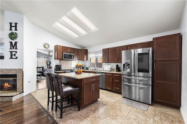 kitchen with appliances with stainless steel finishes, lofted ceiling, a kitchen island, a premium fireplace, and a kitchen breakfast bar