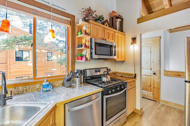 kitchen featuring appliances with stainless steel finishes, hanging light fixtures, light brown cabinetry, sink, and light hardwood / wood-style flooring