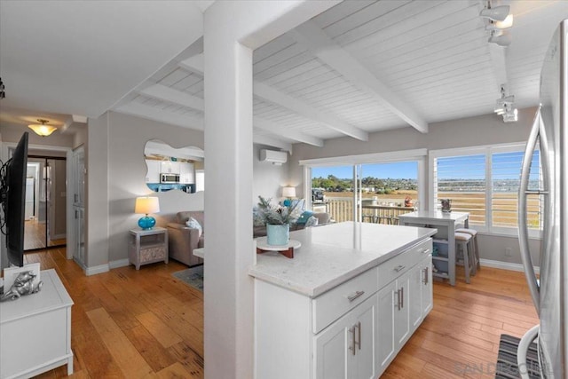 kitchen with white cabinetry, light stone counters, light hardwood / wood-style floors, a wall mounted air conditioner, and beam ceiling