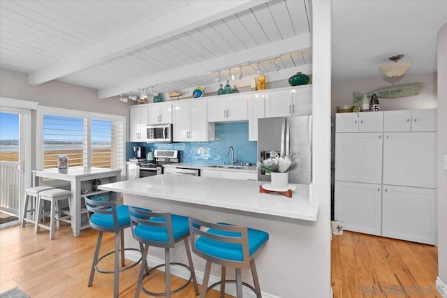 kitchen with decorative backsplash, a breakfast bar area, white cabinets, appliances with stainless steel finishes, and beamed ceiling