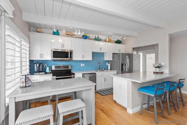 kitchen with a breakfast bar area, appliances with stainless steel finishes, beam ceiling, sink, and white cabinetry