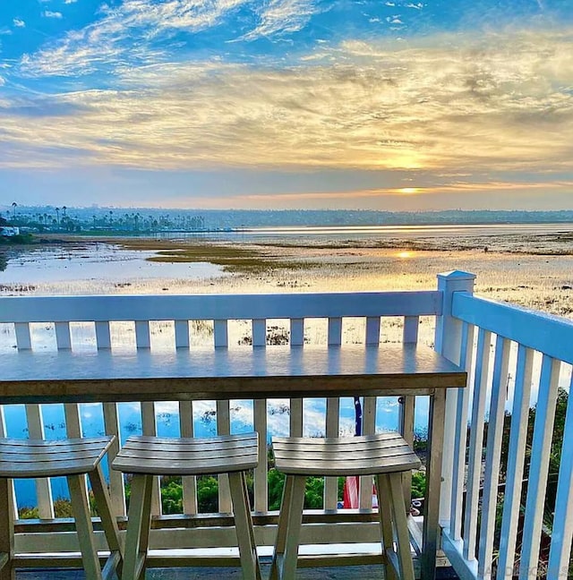 balcony at dusk featuring a view of the beach and a water view