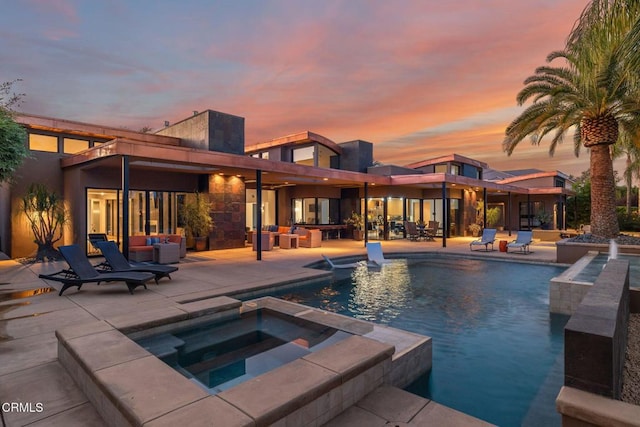 pool at dusk featuring a patio area and an in ground hot tub