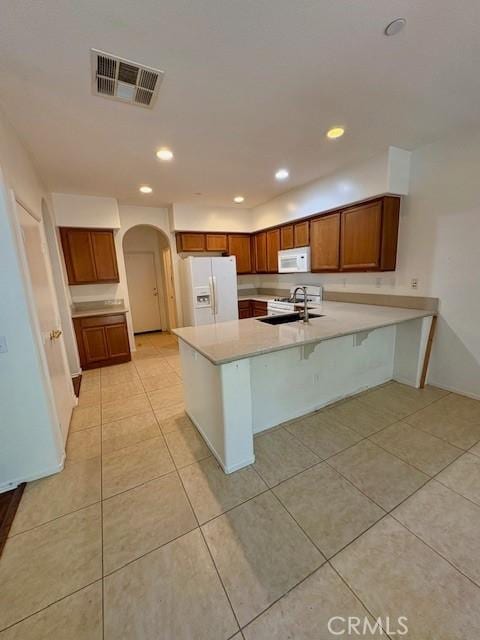 kitchen featuring white appliances, a breakfast bar area, kitchen peninsula, light tile patterned floors, and sink