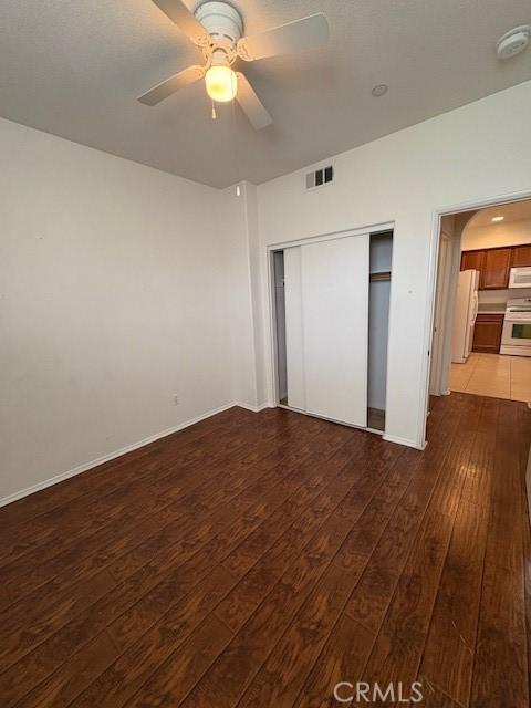 unfurnished bedroom featuring ceiling fan, white refrigerator, hardwood / wood-style floors, and a closet