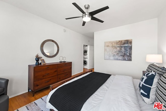 bedroom featuring stacked washing maching and dryer, ceiling fan, and light wood-type flooring