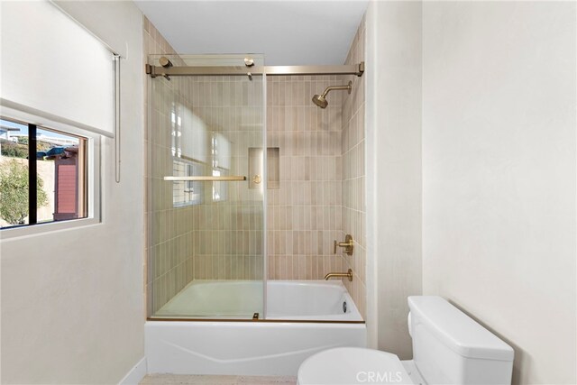 bathroom with toilet and bath / shower combo with glass door