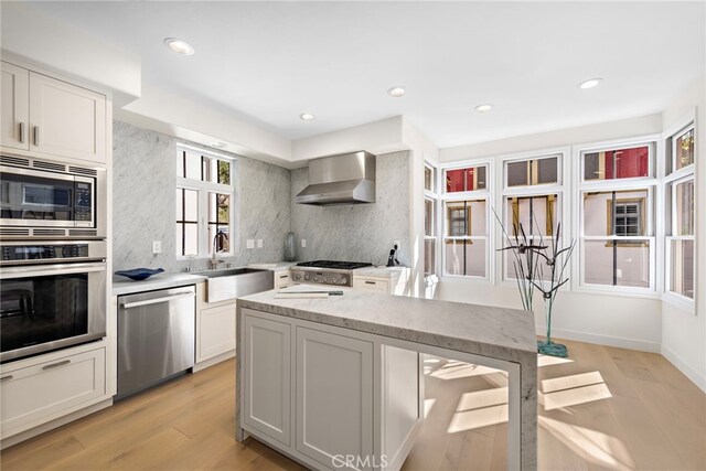 kitchen featuring sink, white cabinetry, wall chimney exhaust hood, light hardwood / wood-style floors, and appliances with stainless steel finishes