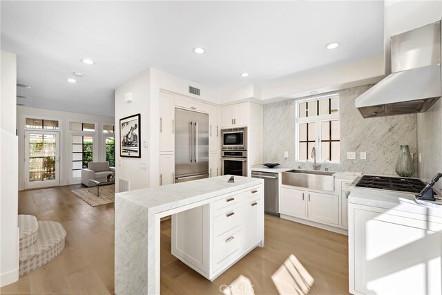 kitchen featuring sink, built in appliances, white cabinetry, wall chimney exhaust hood, and tasteful backsplash