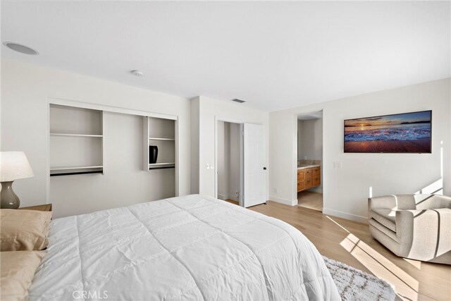 bedroom featuring light wood-type flooring, ensuite bathroom, and a closet