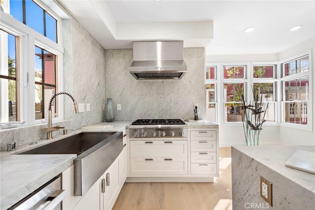 kitchen featuring white cabinets, wall chimney exhaust hood, light hardwood / wood-style flooring, backsplash, and light stone countertops