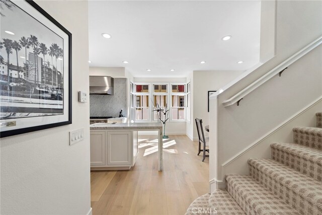 kitchen featuring white cabinets, tasteful backsplash, light hardwood / wood-style flooring, and wall chimney exhaust hood