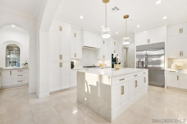 kitchen with stainless steel built in fridge, hanging light fixtures, tasteful backsplash, a kitchen island with sink, and white cabinetry