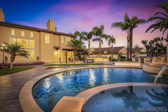 pool at dusk with pool water feature, exterior kitchen, and a patio area