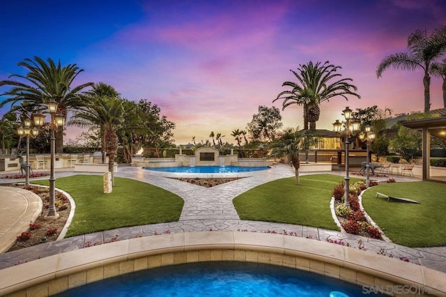 pool at dusk featuring a lawn