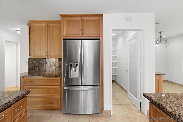 kitchen featuring stainless steel refrigerator with ice dispenser, light tile patterned flooring, and dark stone countertops