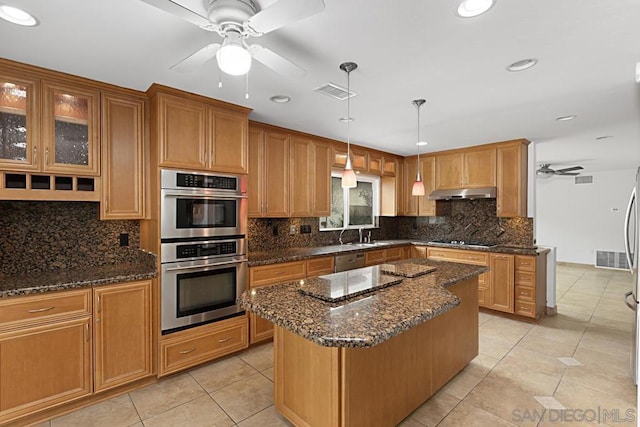 kitchen with appliances with stainless steel finishes, light tile patterned flooring, dark stone countertops, pendant lighting, and a center island