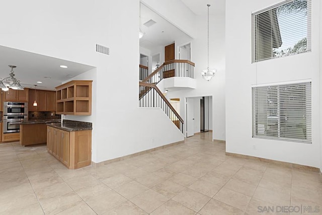 kitchen with decorative light fixtures, a center island, a towering ceiling, an inviting chandelier, and double oven