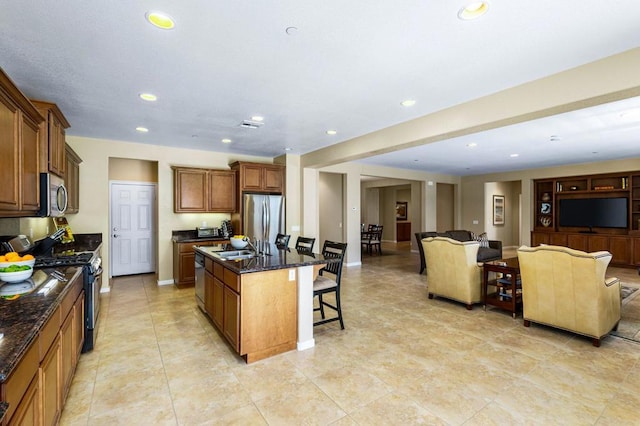 kitchen with a center island with sink, a kitchen breakfast bar, dark stone counters, and appliances with stainless steel finishes