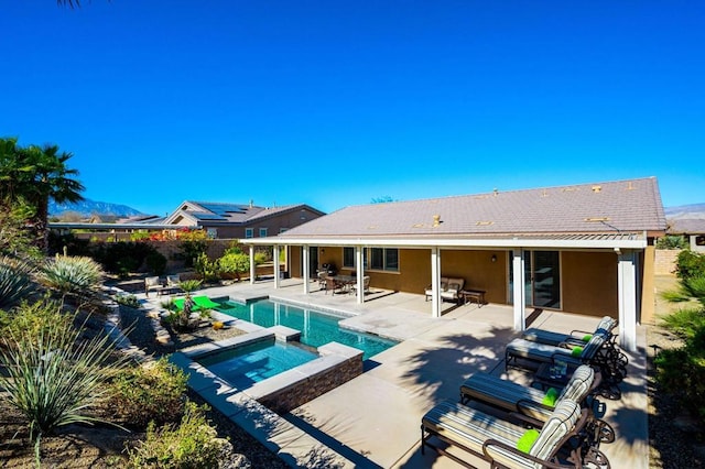 rear view of property featuring a swimming pool with hot tub and a patio area