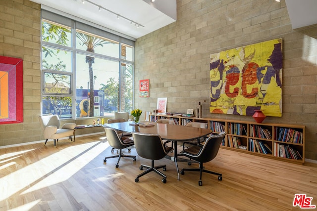 dining room featuring a high ceiling, a wall of windows, track lighting, and hardwood / wood-style floors