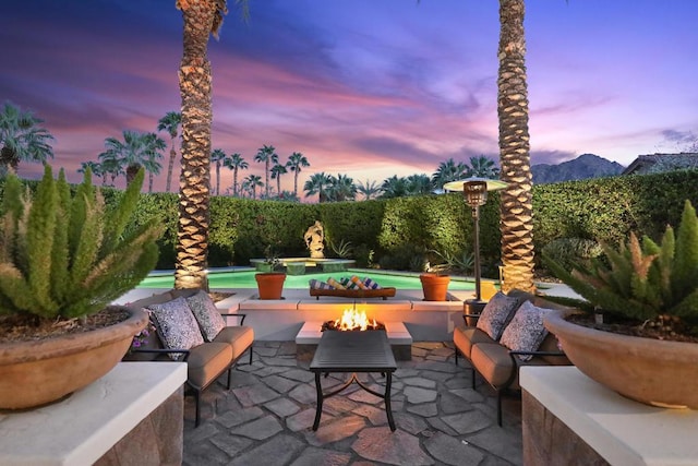 patio terrace at dusk with an outdoor living space with a fire pit, a fenced in pool, and a mountain view