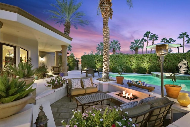 patio terrace at dusk featuring a fenced in pool and an outdoor living space with a fire pit