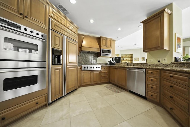 kitchen featuring light tile patterned floors, backsplash, built in appliances, custom range hood, and dark stone counters