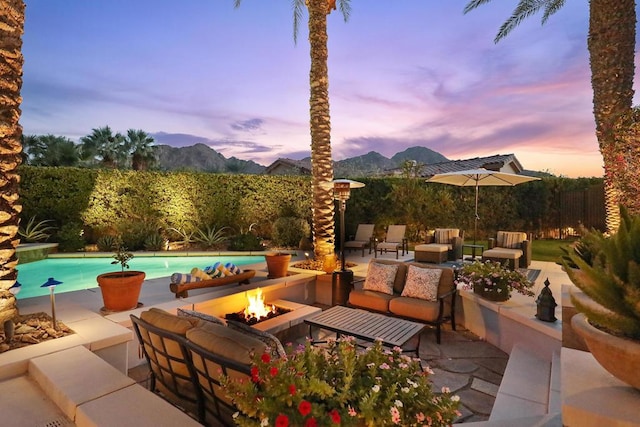 patio terrace at dusk featuring a fenced in pool, a mountain view, and an outdoor living space with a fire pit