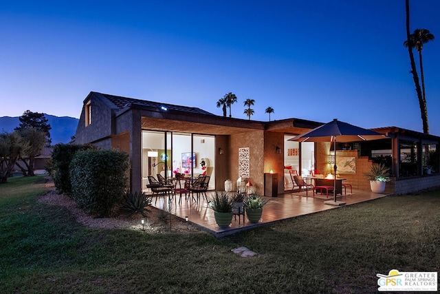 back house at dusk featuring a patio, a yard, and a mountain view