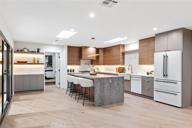 kitchen with a breakfast bar area, white appliances, hanging light fixtures, wall chimney exhaust hood, and a center island